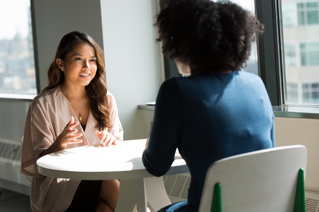 Two women sitting on chairs talking to each other in a corporate environment.